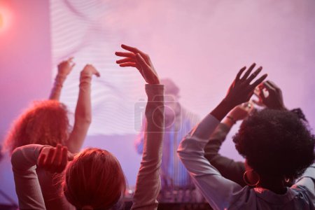 Foto de Vista trasera en grupo de personas bailando en luces de neón en discoteca con DJ en segundo plano - Imagen libre de derechos