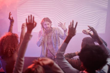 Téléchargez les photos : Portrait de DJ par plaque tournante aux néons acclamant la foule dansante à la soirée disco - en image libre de droit