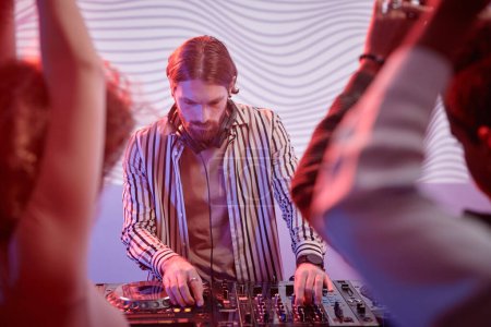 Téléchargez les photos : Portrait de DJ aux cheveux longs par platine dans des néons divertissant public dansant dans une boîte de nuit - en image libre de droit