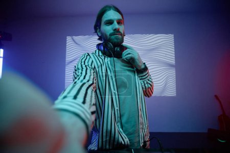 Téléchargez les photos : Point de vue de DJ ou musicien aux cheveux longs prenant des photos selfie dans la lumière au néon, espace de copie - en image libre de droit