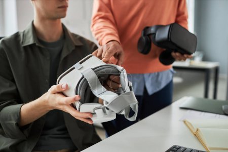 Foto de Primer plano de los desarrolladores jóvenes probando gafas VR y discutiendo el programa de computadora durante el trabajo en equipo en la oficina - Imagen libre de derechos