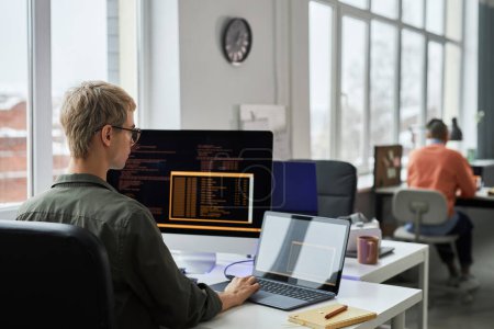 Téléchargez les photos : Jeunes programmeurs écrivant des codes sur ordinateur assis sur leur lieu de travail pendant la journée de travail dans un bureau informatique - en image libre de droit