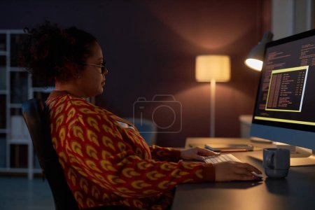 Foto de Mujer afroamericana que trabaja con códigos informáticos mientras trabaja en su lugar de trabajo hasta altas horas de la noche - Imagen libre de derechos