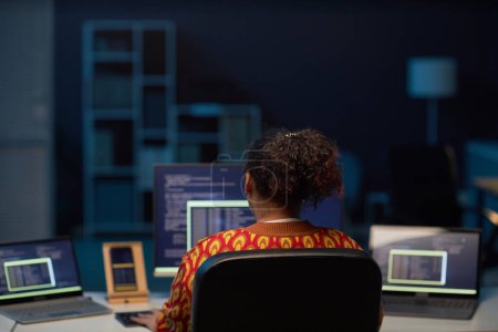 Foto de Vista trasera de una mujer afroamericana que trabaja en computadoras en su lugar de trabajo en la oficina de TI hasta altas horas de la noche - Imagen libre de derechos