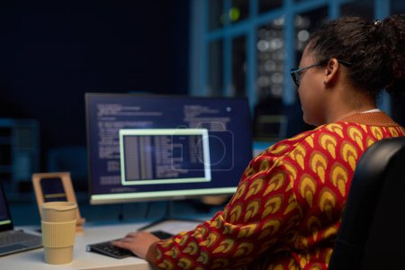 Téléchargez les photos : Vue arrière de programmeuse travaillant avec des codes informatiques sur son lieu de travail jusqu'à tard dans la nuit au bureau - en image libre de droit