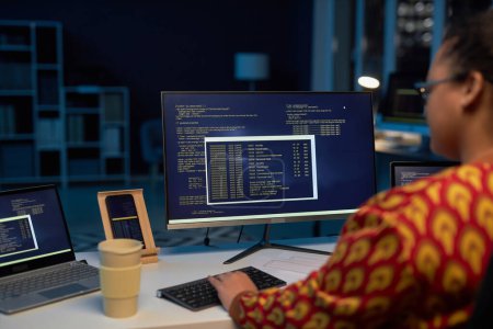 Foto de Vista trasera del programador femenino escribiendo códigos de computadora en el ordenador mientras trabaja hasta altas horas de la noche en la oficina de TI - Imagen libre de derechos