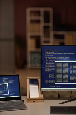 Photo for Vertical image of computers with security codes for program standing on table in dark IT office - Royalty Free Image