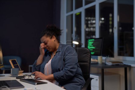Foto de Mujer agotada sentada en su lugar de trabajo con computadora, que trabaja hasta altas horas de la noche en la oficina - Imagen libre de derechos