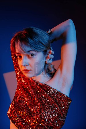 Vertical image of young woman looking at camera while dancing in red dress against blue background