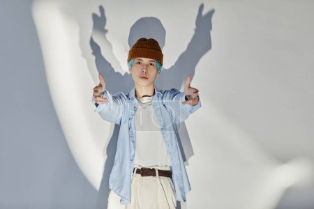 Portrait of professional dancer in stylish clothing looking at camera and showing youth gestures standing on white background