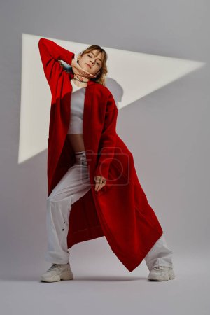 Vertical image of young pretty dancer in red coat exercising on white background