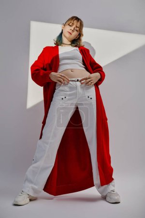 Vertical image of professional dancer in red cardigan looking at camera standing on white background