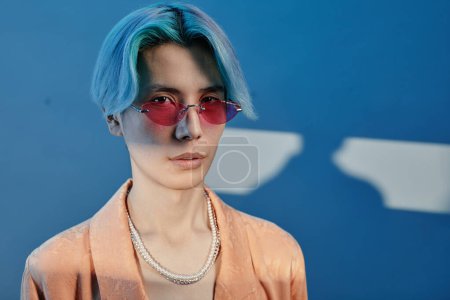 Photo for Portrait of stylish Asian guy with pink sunglasses looking at camera against blue background - Royalty Free Image