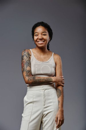 Foto de Retrato vertical de mujer negra confiada con tatuajes mirando a la cámara y sonriendo - Imagen libre de derechos
