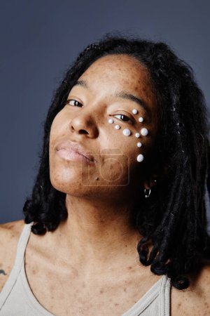 Foto de Retrato vertical de cerca de una joven negra sin maquillaje y perlas como decoración de la cara - Imagen libre de derechos