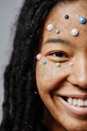 Téléchargez les photos : Demi-visage gros plan de jeune femme noire souriant sans maquillage et perles de perles comme décoration - en image libre de droit