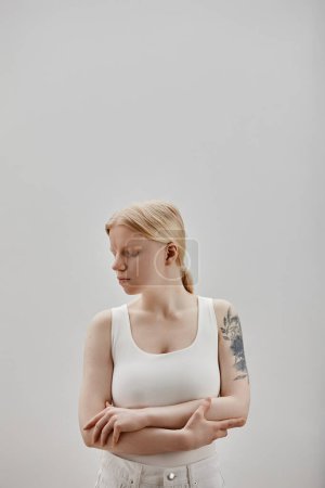 Vertical fashion portrait of ethereal girl with tattooes standing against white background