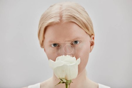 Téléchargez les photos : Portrait minimal de belle jeune fille avec albinisme tenant rose blanche - en image libre de droit