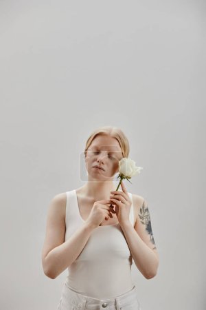 Foto de Retrato vertical de una hermosa joven con albinismo sosteniendo rosa blanca, ojos cerrados - Imagen libre de derechos