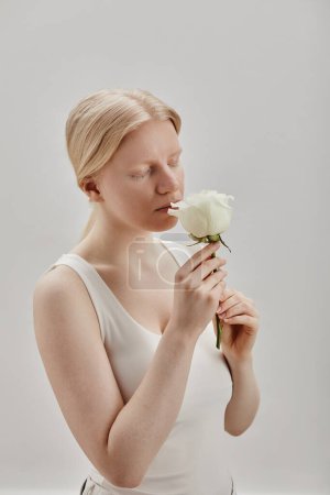 Téléchargez les photos : Portrait vertical minimal de belle jeune femme avec albinisme tenant rose blanche - en image libre de droit