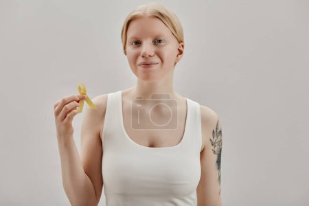 Minimal portrait of young woman with albinism holding yellow ribbon for International awareness day