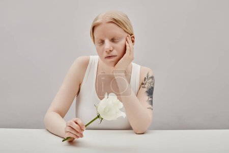 Minimal portrait of young girl with albinism holding white rose, copy space