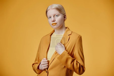 Minimal fashion portrait of young woman with albinism posing against contrasting yellow background