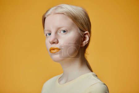 Minimal fashion portrait of young woman with albinism looking at camera against contrasting yellow background
