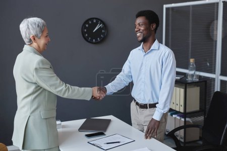 Portrait of smiling HR recruiter shaking hands with senior woman at job interview