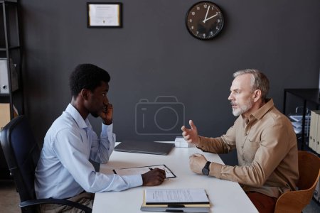 Foto de Retrato de vista lateral del hombre maduro barbudo hablando con el reclutador de recursos humanos en la entrevista de trabajo - Imagen libre de derechos