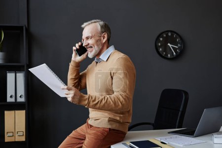 Side view portrait of successful mature man speaking on smartphone in office and looking at window, copy space