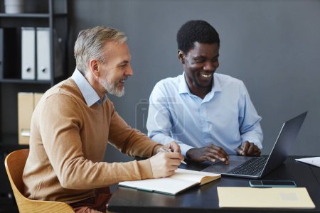 Foto de Retrato de vista lateral del hombre de negocios maduro guapo usando el ordenador portátil con colega en el escritorio en la oficina - Imagen libre de derechos