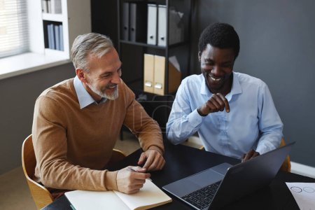 Téléchargez les photos : Portrait d'un jeune homme d'affaires noir avec un collègue aîné utilisant un ordinateur portable ensemble sur le lieu de travail au bureau - en image libre de droit