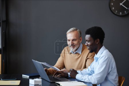 Photo for Side view portrait of black young businessman with senior colleague collaborating at workplace in office, copy space - Royalty Free Image