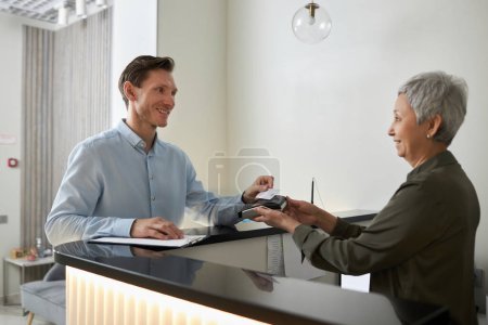 Téléchargez les photos : Portrait d'un homme élégant souriant payant dans une clinique médicale via la technologie NFC, espace de copie - en image libre de droit