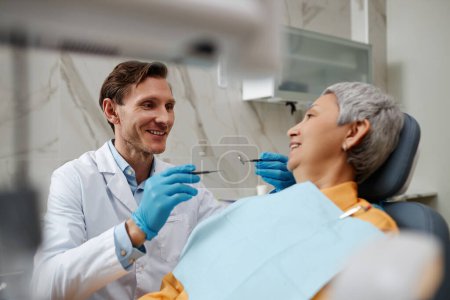 Foto de Retrato del dentista masculino sonriente examinando a la mujer mayor durante el chequeo dental en la clínica - Imagen libre de derechos