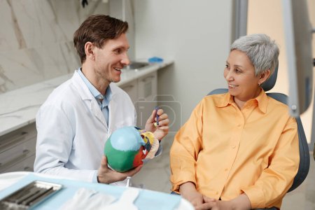 Foto de Retrato de vista lateral del dentista masculino amigable hablando con la mujer mayor sonriente durante la consulta en la clínica dental - Imagen libre de derechos