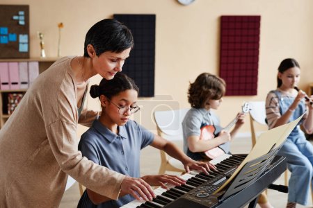 Téléchargez les photos : Enseignant professionnel apprenant aux enfants à jouer des instruments de musique en classe de musique - en image libre de droit