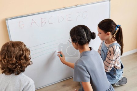 Téléchargez les photos : Vue arrière d'un groupe d'enfants écrivant sur un tableau blanc et apprenant des notes ensemble en classe de musique - en image libre de droit