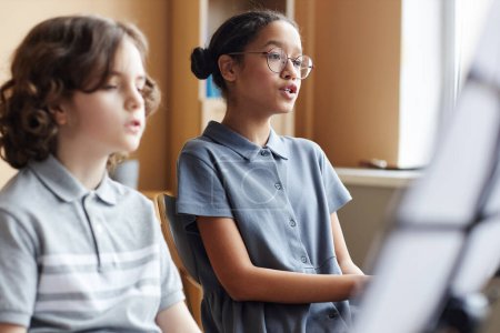 Téléchargez les photos : Groupe d'enfants chantant des chansons assis devant des notes pendant les cours de musique en classe - en image libre de droit