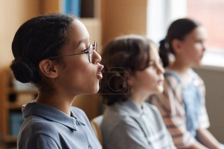 Photo for Side view of African American schoolgirl singing song together with other children in music class - Royalty Free Image