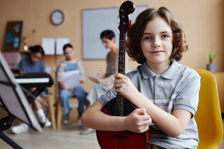 Téléchargez les photos : Portrait de petit garçon avec instrument de musique regardant la caméra tout en étudiant en classe de musique - en image libre de droit