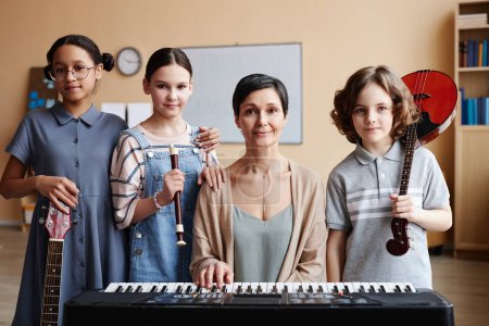 Photo for Portrait of teacher sitting at piano and looking at camera together with children in music class - Royalty Free Image