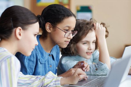 Photo for Children working over online presentation in team using laptop while sitting at table together during lesson - Royalty Free Image