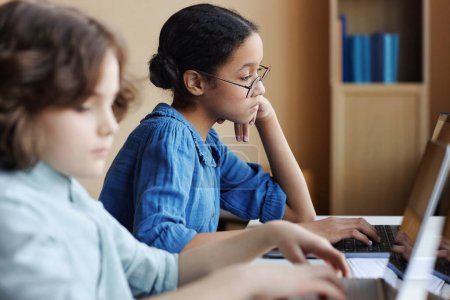 Téléchargez les photos : Les écoliers se concentrent sur le travail sur ordinateur alors qu'ils sont assis à table pendant la leçon de technologie de l'information - en image libre de droit