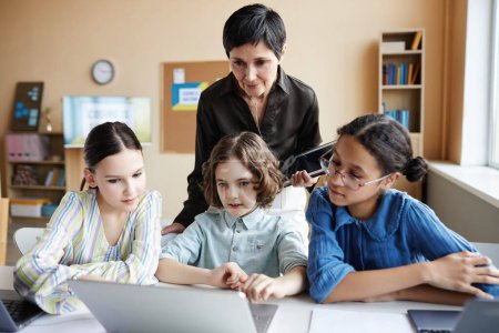 Téléchargez les photos : Enseignant aidant groupe d'enfants avec présentation en ligne sur ordinateur pendant les cours à l'école - en image libre de droit