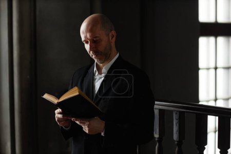 Foto de Hombre maduro en traje concentrado en leer la Biblia mientras ora en la iglesia bautista - Imagen libre de derechos