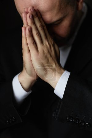 Foto de Imagen vertical del hombre maduro en traje negro rezando con los ojos cerrados - Imagen libre de derechos
