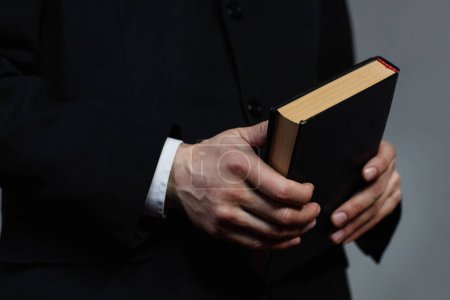 Close-up of pastor in black suit holding Bible book during sermon in church