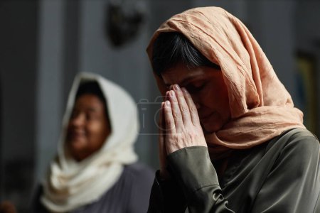 Foto de Mujer madura con pañuelo en la cabeza rezando durante su visita a la iglesia - Imagen libre de derechos